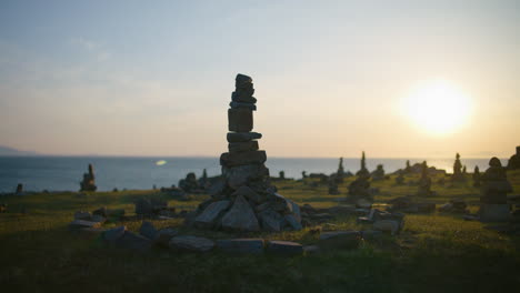Stacked-stones-in-a-field-at-sunset-by-the-sea,-creating-a-serene-and-peaceful-atmosphere
