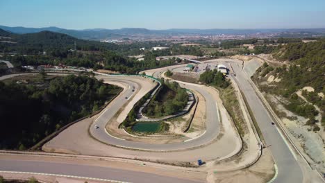 Castelloli-speed-circuit-in-barcelona-on-a-sunny-day-with-winding-track-and-lush-landscape,-aerial-view