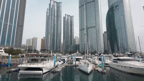 Stunning-high-definition-footage-of-a-luxurious-yacht-moored-at-a-bustling-port,-with-a-backdrop-of-towering-city-skyscrapers,-capturing-the-essence-of-urban-coastal-luxury