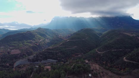 Mountainous-landscape-with-winding-roads-and-sunlight-breaking-through-the-clouds