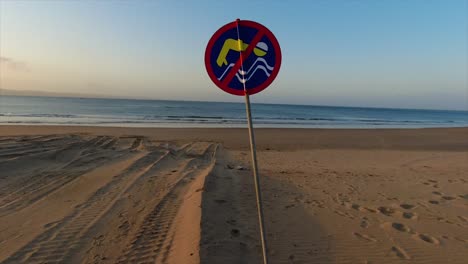 Vista-En-Movimiento-De-Una-Señal-De-No-Nadar-En-Azul,-Amarillo-Y-Rojo-En-Una-Playa-De-Arena-Desierta-Con-Un-Fondo-Claro