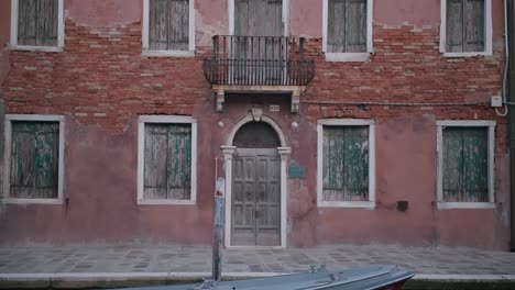 Weathered-building-facade-in-Burano-Island,-Venice,-featuring-rustic-brickwork-and-aged-wooden-shutters,-exuding-an-old-world-charm