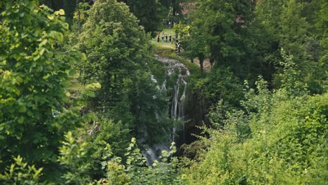 Lush-greenery-with-a-waterfall-in-the-background-and-people-enjoying-the-scenic-views-in-Rastoke,-Croatia