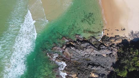 4K-Drone-video-flying-higher-over-a-beautiful-beach-with-blue-ocean-waves,-soft-white-sand-and-grey-cliff-rock-formations-in-Noosa,-Queensland-Australia