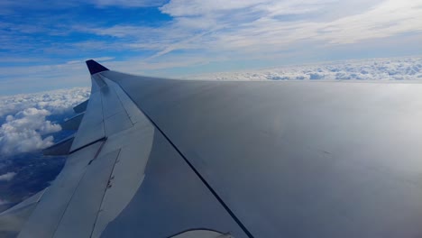 Airplane-wing-with-beautiful-snowy-white-clouds-and-blue-sky-on-sunny-day-view-through-aircraft-window