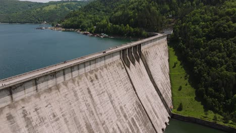 Dam-and-water-reservoir-surrounded-by-green-forests,-panoramic-aerial-view