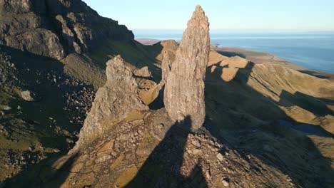 Ancient-volcanic-plug-stone-spire-The-Old-Man-of-Storr-bathed-in-early-morning-winter-sunshine-with-reveal-of-lowlands-and-coastline