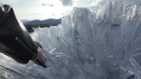 Person-touching-large,-intricate-ice-formations-with-afternoon-sunlight-illuminating-the-scene-in-a-mountainous-area