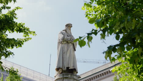 Historic-Leonardo-Davinci-statue-framed-by-lush-green-leaves-in-Milan,-Italy