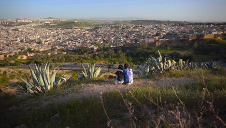 Una-Pareja-Aventurera-De-Hombre-Y-Mujer-Sentada-En-La-Ladera-Seca-Con-Vistas-A-Fez,-Marruecos