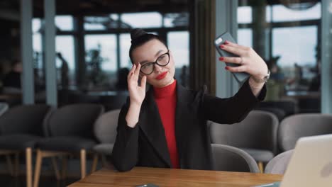 beautiful-woman-in-business-attire-takes-a-selfie-with-her-smartphone-while-sitting-in-a-restaurant