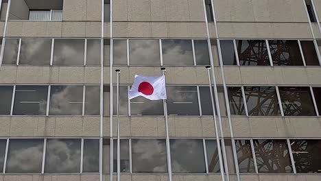 Bandera-Nacional-De-Japón-Ondeando-En-La-Fachada-De-Cristal-De-Un-Edificio-Moderno.