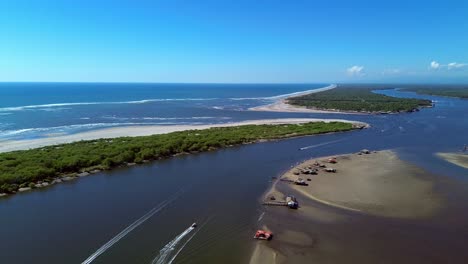Panoramic-aerial-view-of-the-mouth-that-connects-the-estuary-and-the-Pacific-Ocean-sunny-day-with-boats-in-the-panorama
