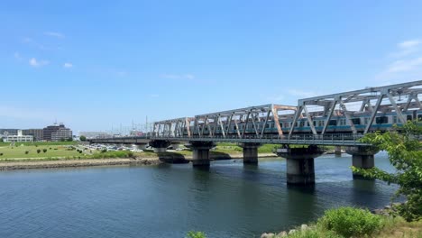 Stahlbrücke-über-Einen-Fluss-An-Einem-Sonnigen-Tag-Mit-Stadtbild-Im-Hintergrund