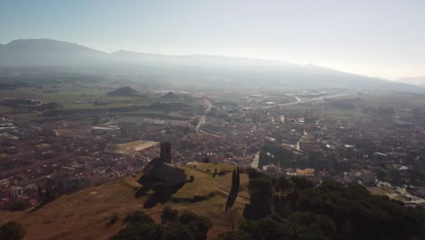 Tona's-hermitage-with-the-town-and-distant-mountains-in-the-background,-aerial-view