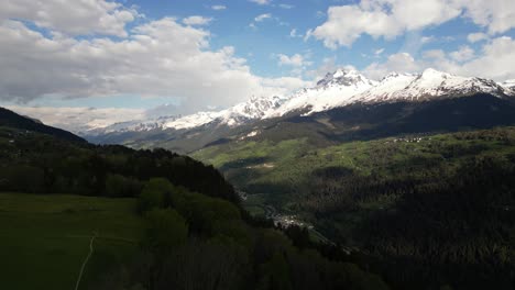 Vista-Aérea-Del-Valle-En-Obersaxen,-Graubünden,-Suiza,-Rodeado-Por-Una-Cadena-Montañosa-Con-Picos-Cubiertos-De-Nieve.