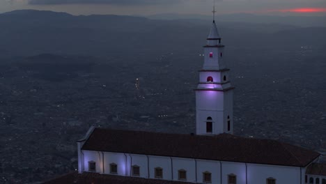 Drone-shot-of-Monserrate-church-overlooking-the-city-of-Bogota,-Colombia-at-blue-hour