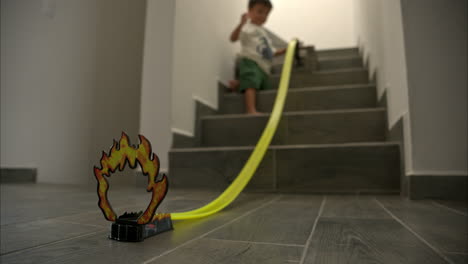 Young-mexican-latin-boy-playing-sliding-his-car-toys-on-a-track-downstairs-having-great-fun-in-slow-motion