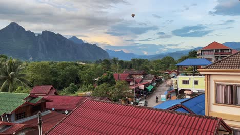 Timelapse-of-the-small-town-of-Vang-Vieng-in-Laos,-with-hot-air-balloons-swiftly-passing-and-a-breathtaking-landscape-in-the-background