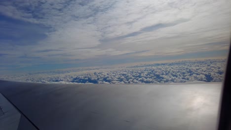 Dynamic-view-of-airplane-wing-flying-and-tilting-above-beautiful-cotton-like-clouds