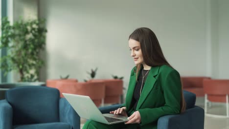 Charmante-Frau-Startet-Einen-Videoanruf-Und-Winkt-Mit-Der-Hand-Zum-Laptop,-Während-Sie-In-Der-Lobby-Eines-Business-Centers-Sitzt