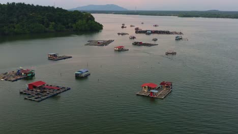 Aerial-view-drone-flyover-capturing-traditional-floating-fish-farms-on-calm-waters,-the-wooden-structures-with-cages-and-nets-are-used-for-aquaculture