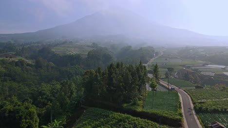 Pequeña-Carretera-En-El-Campo-Y-Las-Tierras-De-Cultivo-De-Indonesia,-El-Volcán-Sumergido-En-El-Fondo