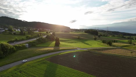 Sunset-over-lush-green-fields-and-a-road-winding-through-Greifensee,-Switzerland