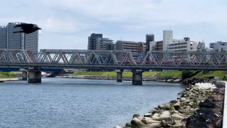 A-train-crosses-a-bridge-over-a-river-in-an-urban-cityscape-under-a-clear-sky