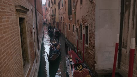 Narrow-Venetian-canal-bustling-with-gondolas,-surrounded-by-historic-brick-buildings