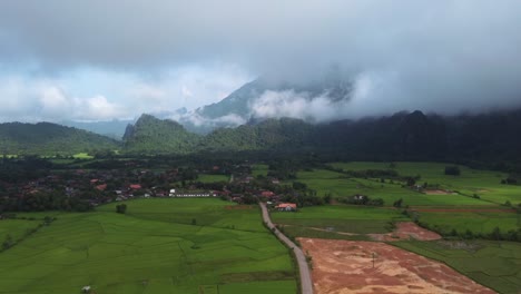 Bird's-eye-view-advancing-over-a-valley-in-Laos,-showcasing-its-beautiful-green-mountains-and-vast-rice-plantations