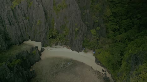 Rocky-forested-cliffs-and-sand-beach-in-Philippines,-aerial-push-in