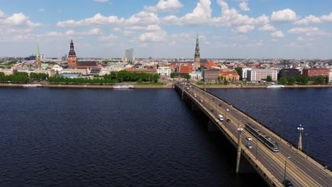 Forward-Drone-Shot-Above-Stone-Bridge-in-Riga,-Latvia-as-Tram-Travels-Downtown