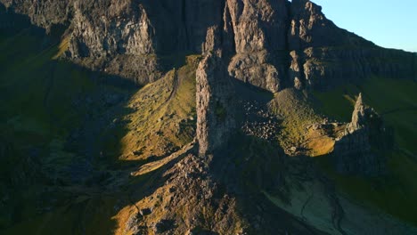 Ancient-volcanic-plug-stone-spire-The-Old-Man-of-Storr-early-morning-in-winter-with-pullback-reveal-of-crumbling-stone-cliffs-of-The-Storr,-Isle-of-Skye,-Western-Highlands,-Scotland,-UK