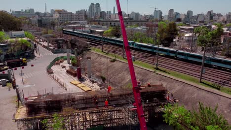 Train-passes-construction-site-in-sunny-Buenos-Aires,-aerial-push-in