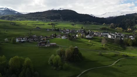 Aerial-view-of-a-small-residential-settlement-nestled-in-the-lush-natural-greenery-of-Obersaxen,-Graubünden,-Switzerland,-showcasing-serene-alpine-living