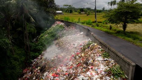 Waste-disposal-next-to-country-road-in-Bali,-smoldering-garbage-pile