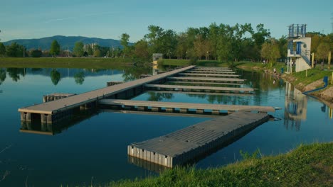 Muelles-Modernos-Que-Se-Extienden-Hacia-Un-Lago-Tranquilo-Con-Reflejos-Y-Montañas-Distantes-En-El-Lago-Jarun,-Zagreb,-Croacia.