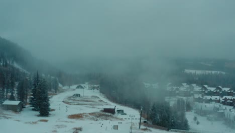 Drone-zoom-forward-over-snow-covered-buildings-into-dense-fog,-4K