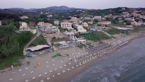 Aerial-fly-in-view-of-a-Greek-Beach-revealing-apartments,-villas-and-restaurant-during-twilight-Corfu-Greece