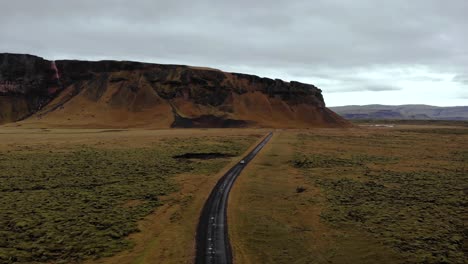 Aerial-4k-view-of-a-car-driving-on-a-dirty-road-surrounded-by-green-moss-lava-field-with-a-beautiful-mountain-landscape,-Iceland,-Europe,-Drone-tripod-shot