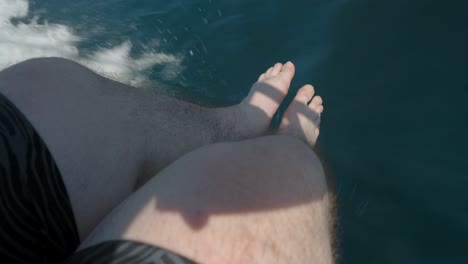 Man-legs-relaxing-over-the-edge-of-a-cruising-boat,-dramatic-shadows