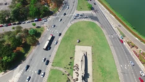 Aerial-drone-vertical-panorama-from-Victor-brecheret-sculpture-in-the-roundabout-with-cars-passing-on-both-sides-showing-lake-in-the-Ibirapuera-park-with-sao-paulo-buildings-skyline