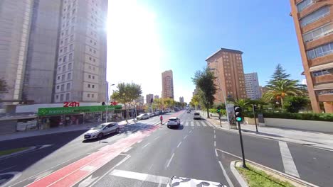 Cars-speeding-on-empty-road-with-a-halt-at-the-traffic-signal-during-a-bright-sunny-day-in-city-surrounded-by-tall-buildings,-shops-and-stores