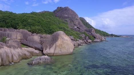 Drone-tracking-shot-of-beautiful-tropical-beach-in-La-Digue,-Seychelles,-under-a-blue-sky-with-turquoise-water