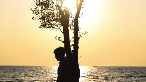 Silhouette-Eines-Männlichen-Reisenden,-Der-Am-Strand-Von-Guliakhali-Vor-Dem-Orangefarbenen-Sonnenuntergangshimmel-An-Einem-Baum-Vorbeigeht