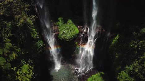 Going-down-aerial-view-on-the-Air-Terjun-Fiji-waterfalls-with-rainbow-reflection-in-middle-of-rain-forest,-one-of-the-most-famous-popular-and-beautiful-destinations-while-travel-to-Bali,-Indonesia