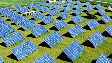 A-solar-farm-with-rows-of-blue-solar-panels-on-green-grass,-aerial-view