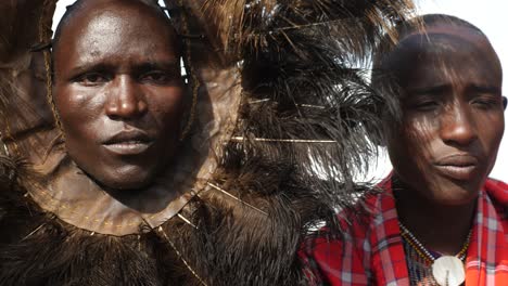 Guerrero-Masai-Con-Plumas-De-Avestruz-En-La-Cabeza-De-Cerca-Cantando-Su-Canción-Tradicional-En-Kenia-Alrededor-De-Su-Aldea-Con-Trajes-Tribales-Tradicionales