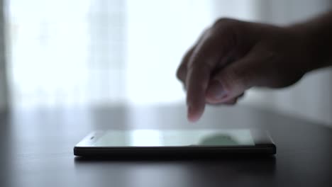 Nahaufnahme-Einer-Männlichen-Hand,-Die-Mit-Einem-Smartphone-Den-Touchscreen-Auf-Dem-Tisch-Scrollt